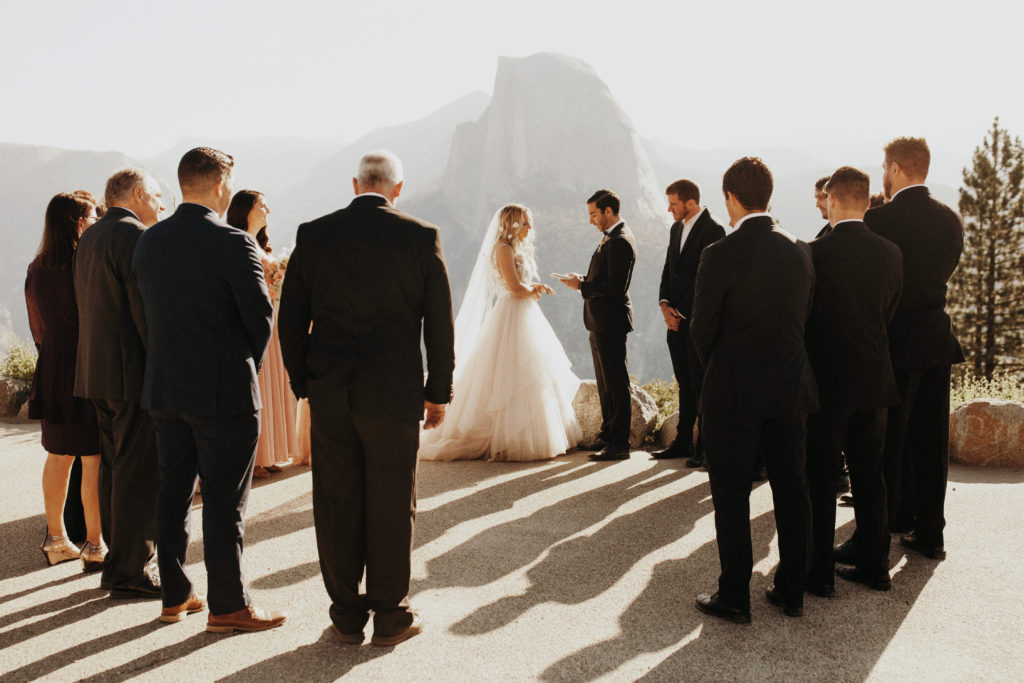 Wedding members and guests gather in a circle as the bride and groom exchange vows in front of Half Dome, in Yosemite National Park.