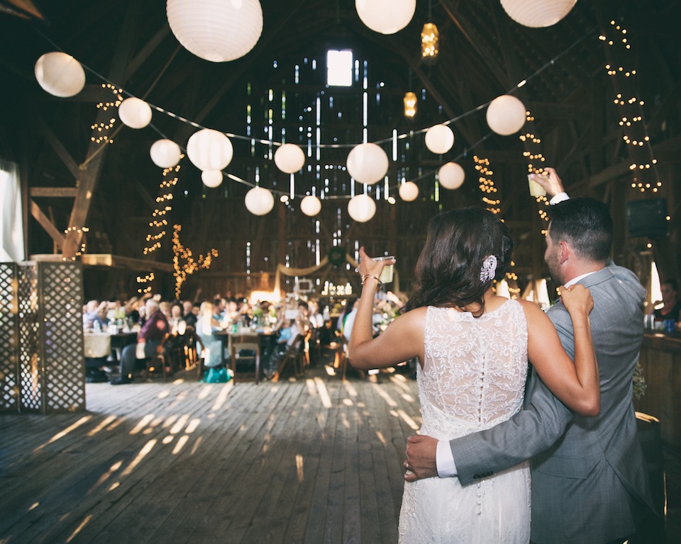 bride and groom cheers to their wedding guests in a barn