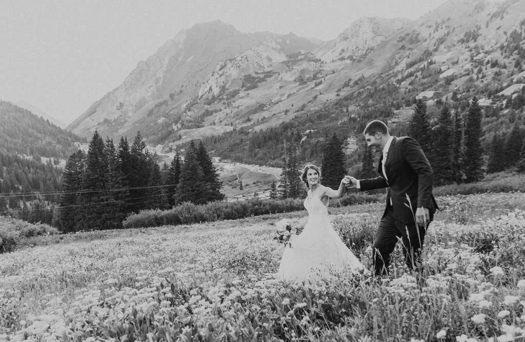 Couple holds hand and runs through a bed of wildflowers in the Wasatch Mountains