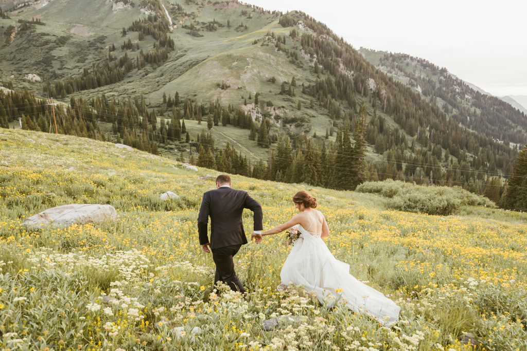 wedding couple walking through wildflowers with mountains around them