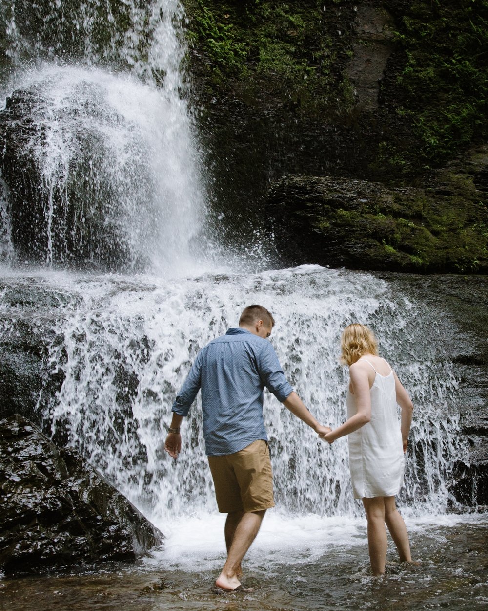 Couple walking in water under waterfall holding hands in Upstate, NY