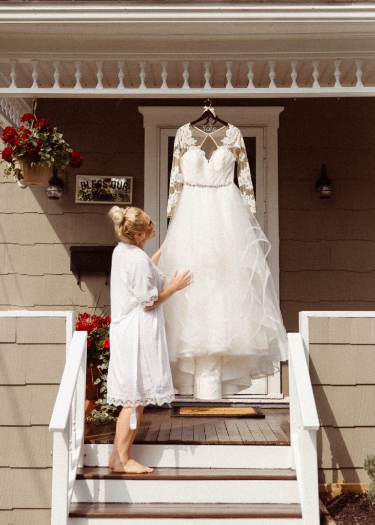 bride admires wedding dress hanging on her front porch