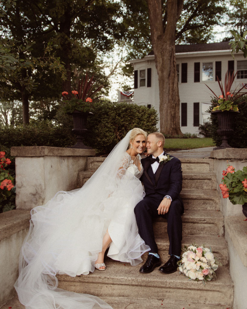 bride and groom sit on steps on their wedding day in the village of Baldwinsville, NY