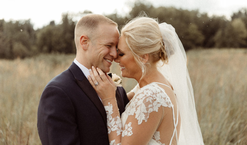 bride and groom nuzzle in field