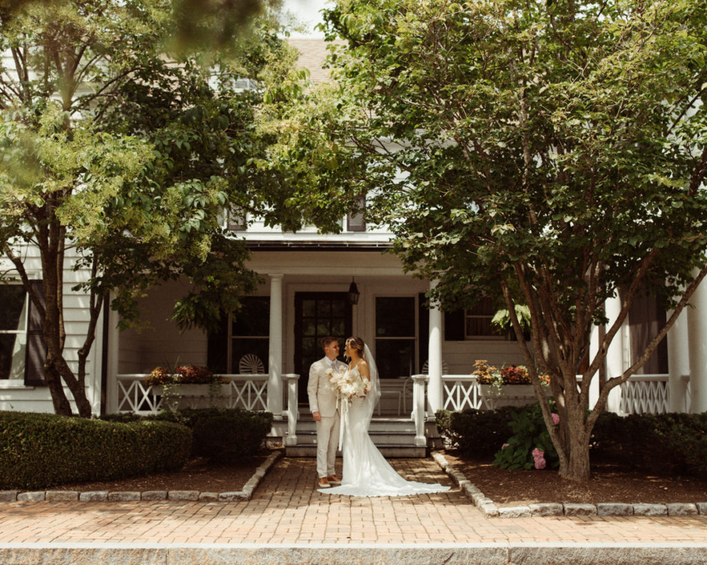 A couple is standing in front of the Hobbit Hollow wedding venue in the Finger Lakes. They're facing each other and smiling.