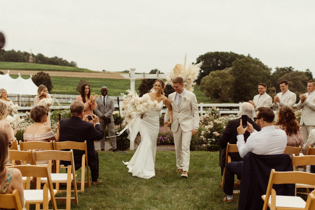 A couple is holding hands, walking away from their ceremony at the Hobbit Hollow wedding venue in the Finger Lakes.