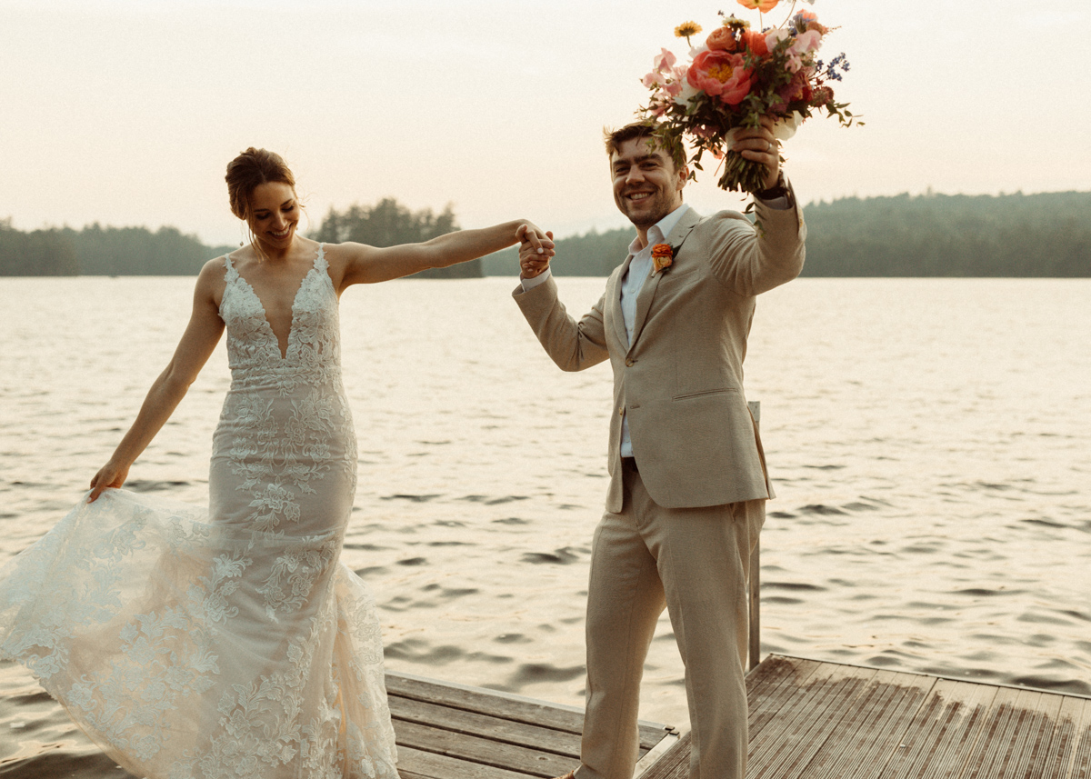 Bride and groom dance on a dock with Tupper Lake and the Adirondack Mountains behind them.