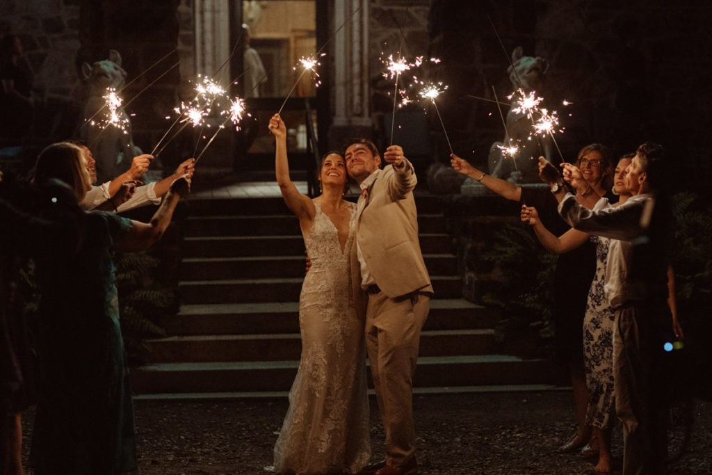 A sparkler exit at an intimate wedding. The bride and groom stand in the middle looking up, as their limited guests stand around them smiling and holding up sparklers too.