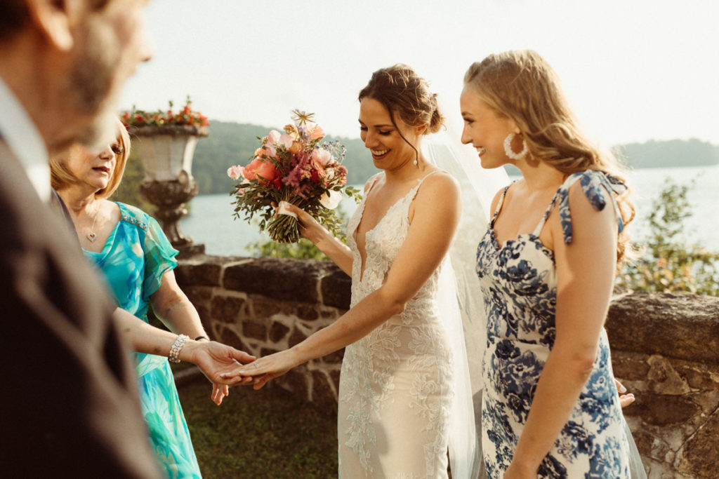 At an intimate wedding, the four guests gather around to look at the bride's wedding ring. She holds her colorful bouquet and everyone is smiling.