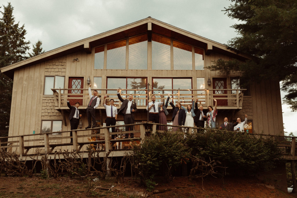 Wedding guests wave from the deck of their airbnb wedding in the Adirondacks NY.