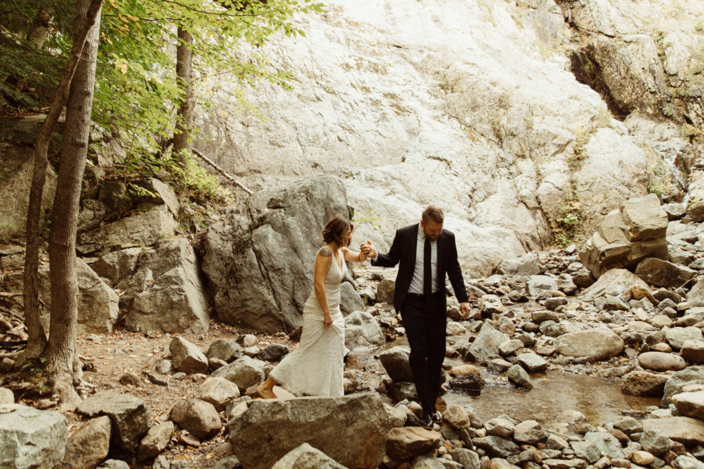 A couple is crossing a stream during their elopement in the Adirondacks.