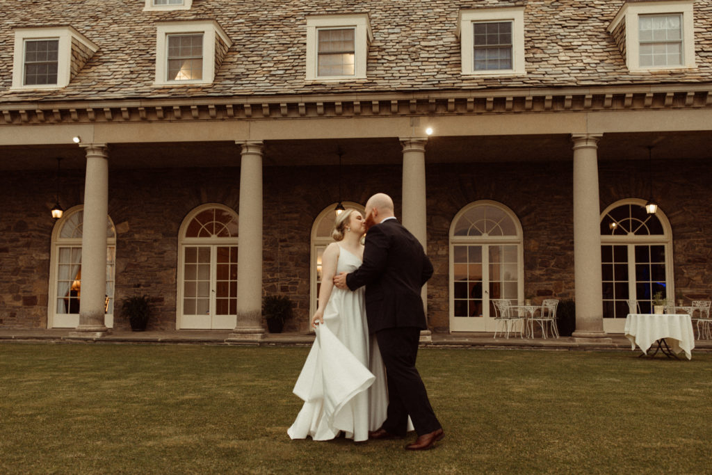 A couple kissing in front of the Onondaga Golf and Country Club, one of the best wedding venues in Syracuse.