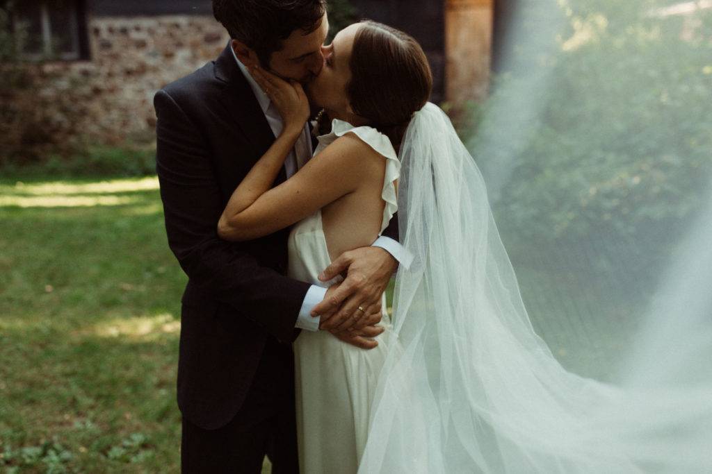 A wedding couple kisses in front of a stone wall barn in the Catskills region of NY.