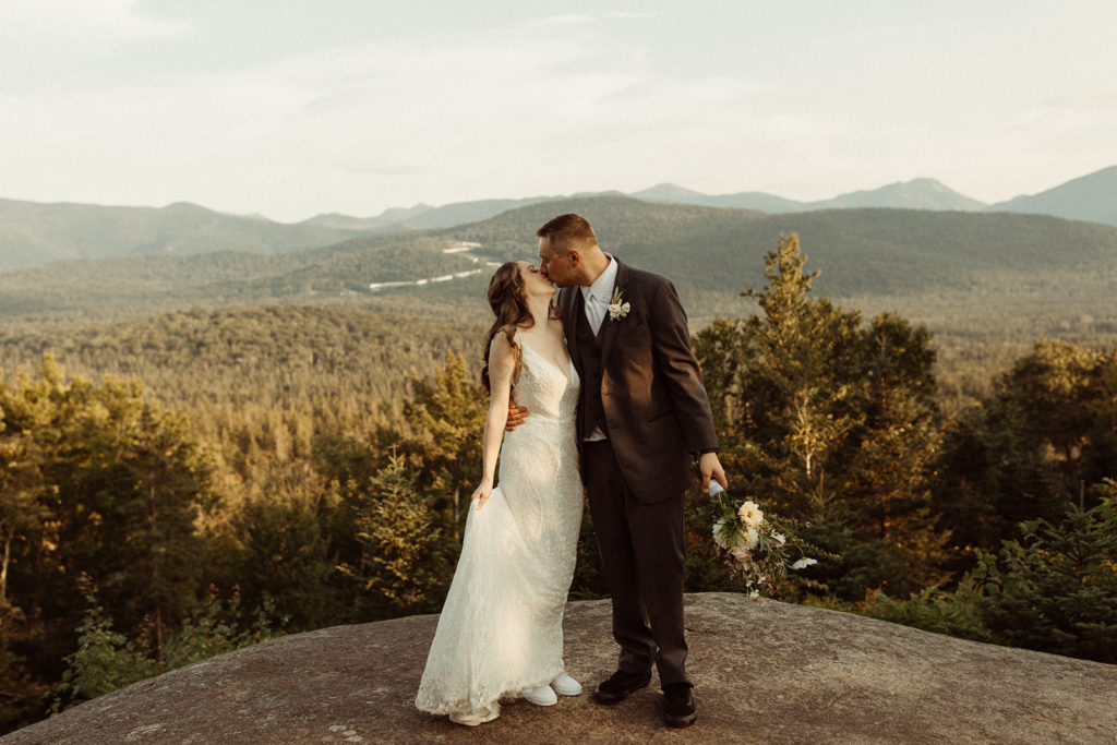Wedding couple standing on rock cliff with Adirondack mountains in background. This area is a popular region for weddings in New York state.